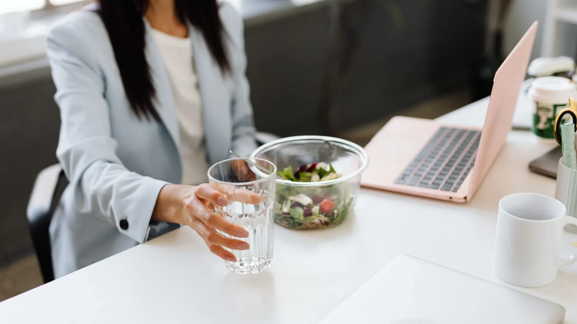 Confident professional smiling at a desk with a healthy meal and water, suggesting long-term balance between work demands and gut health.