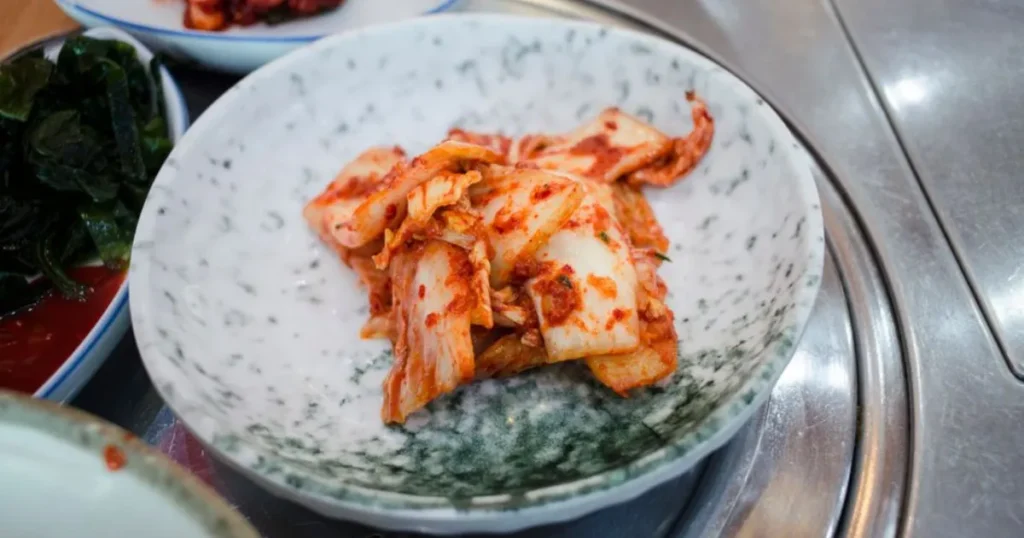 A bowl of homemade kimchi with a chopstick, representing the daily kimchi benefits for gut health and its probiotic power.