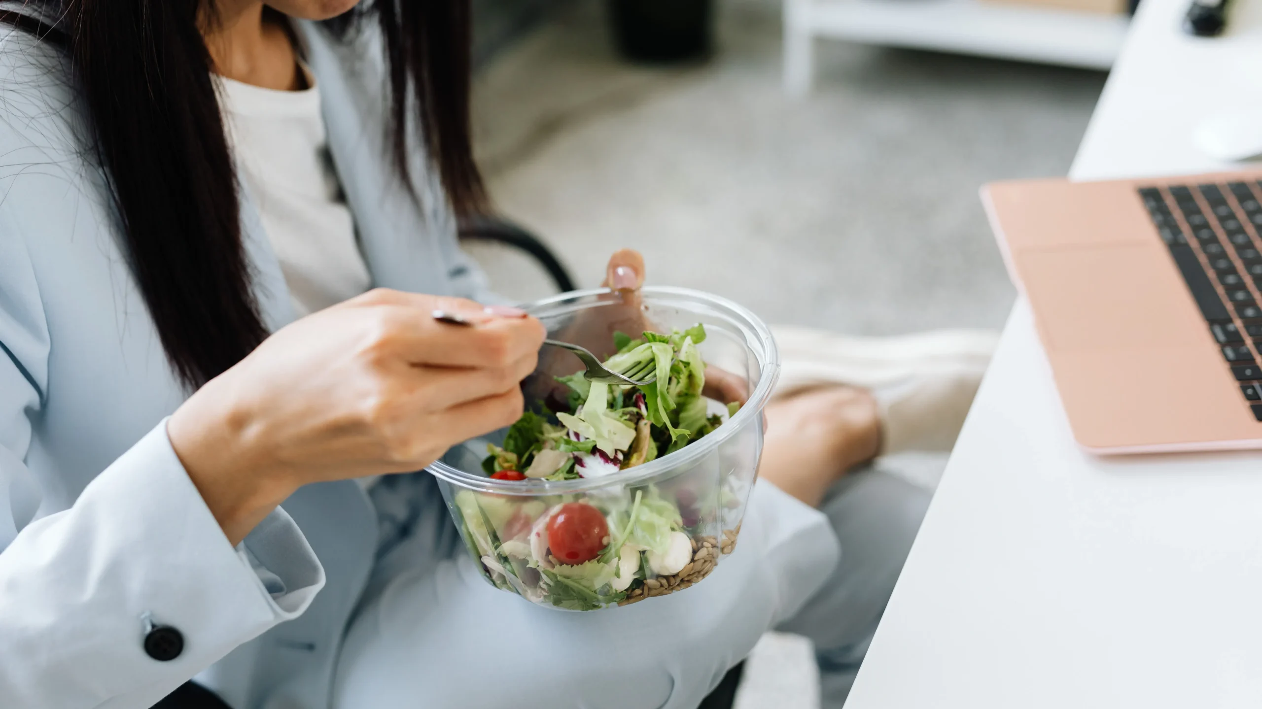 Office desk with laptop, notebook, and a lunch tray containing salad, fruit, and water, illustrating Day 1 of a gut health plan.
