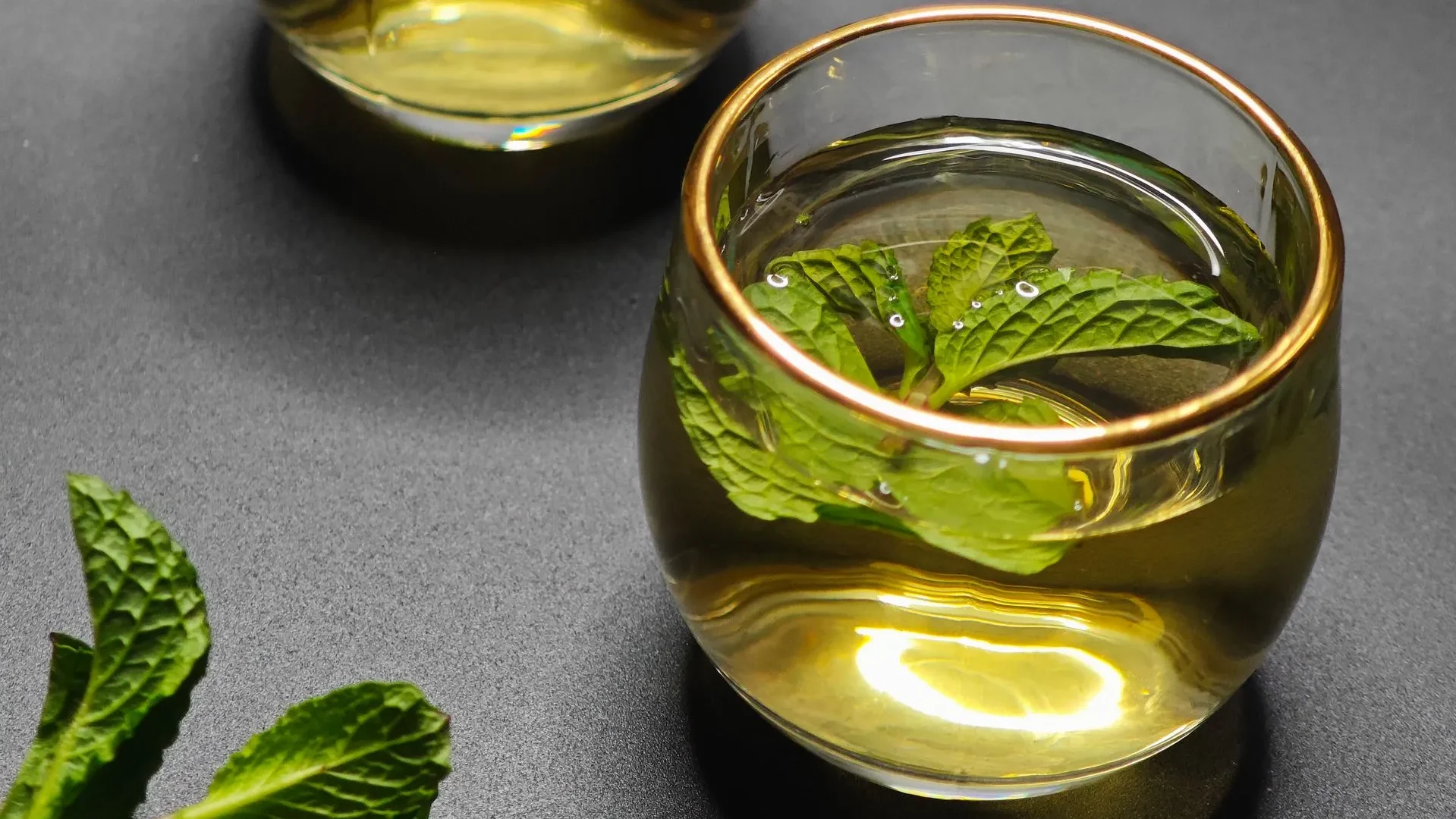  Clear glass mug of peppermint tea with fresh leaves, a caffeine-free drink for gut health that soothes the digestive tract and relaxes muscles.