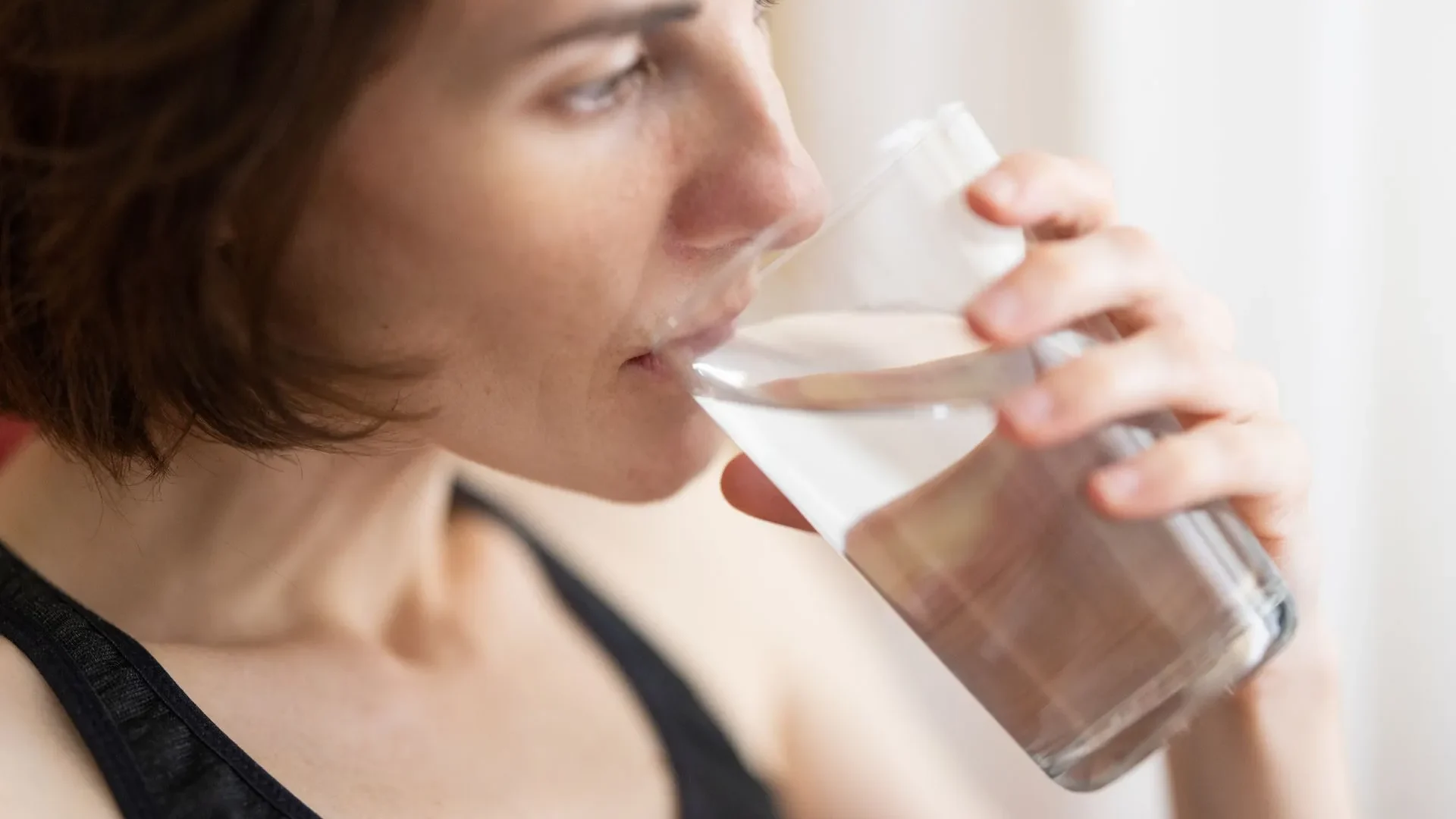 Woman drinking water from a glass, with a cup of green tea and a small bowl of bone broth on the table, supporting digestion and gut lining.