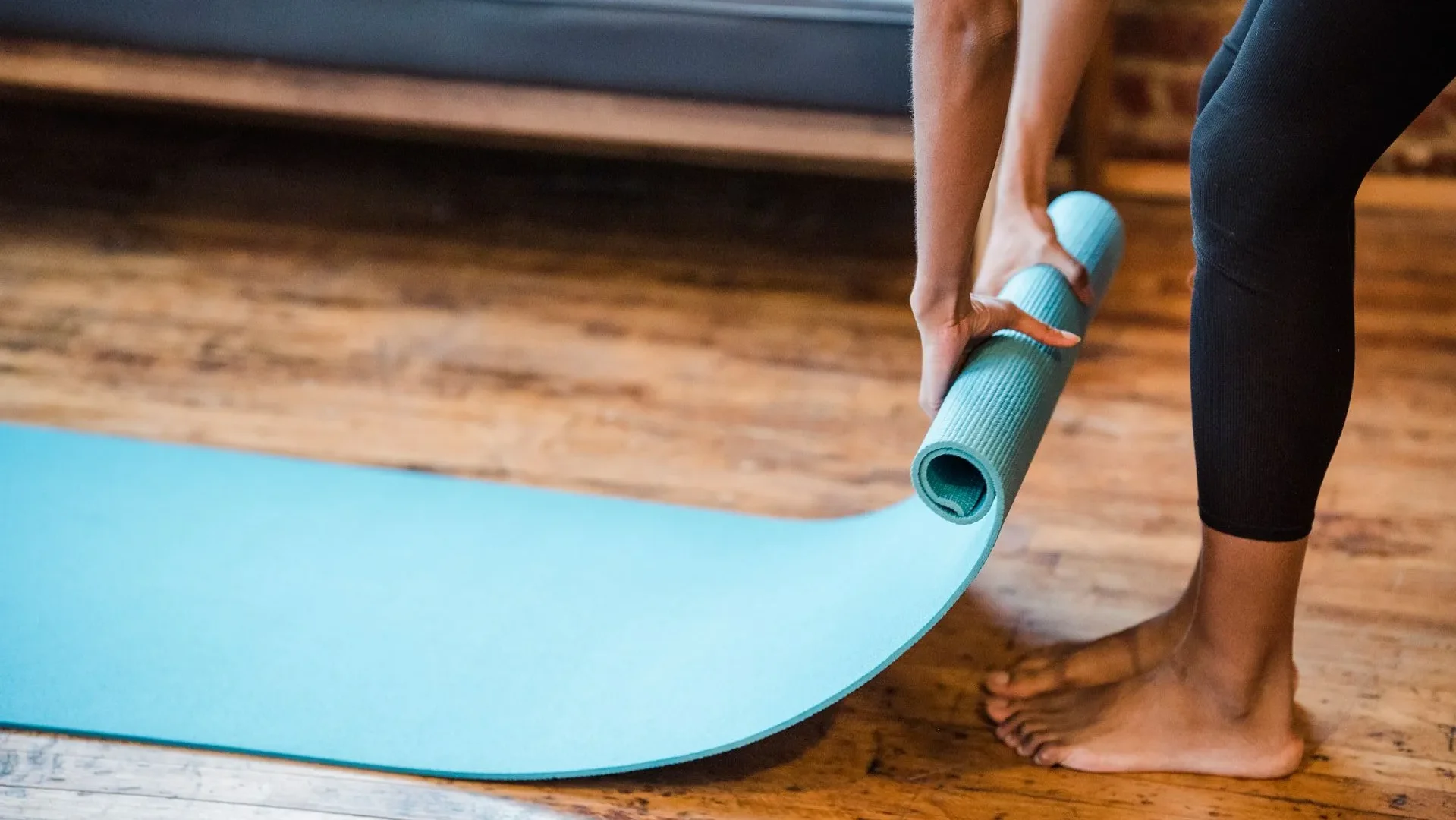 Happy woman rolling up a yoga mat after a session, symbolizing the holistic digestive benefits of consistent yoga for gut health.