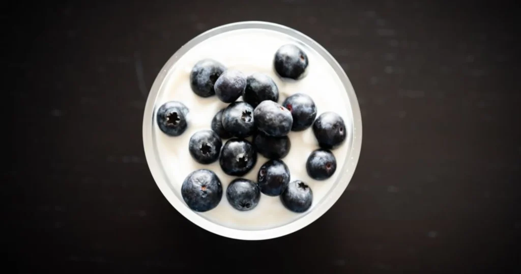 A bowl of plain yogurt topped with fresh berries and a spoon, highlighting the yogurt benefits for gut health as part of a daily diet.