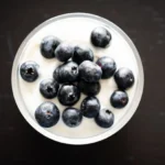 A bowl of plain yogurt topped with fresh berries and a spoon, highlighting the yogurt benefits for gut health as part of a daily diet.